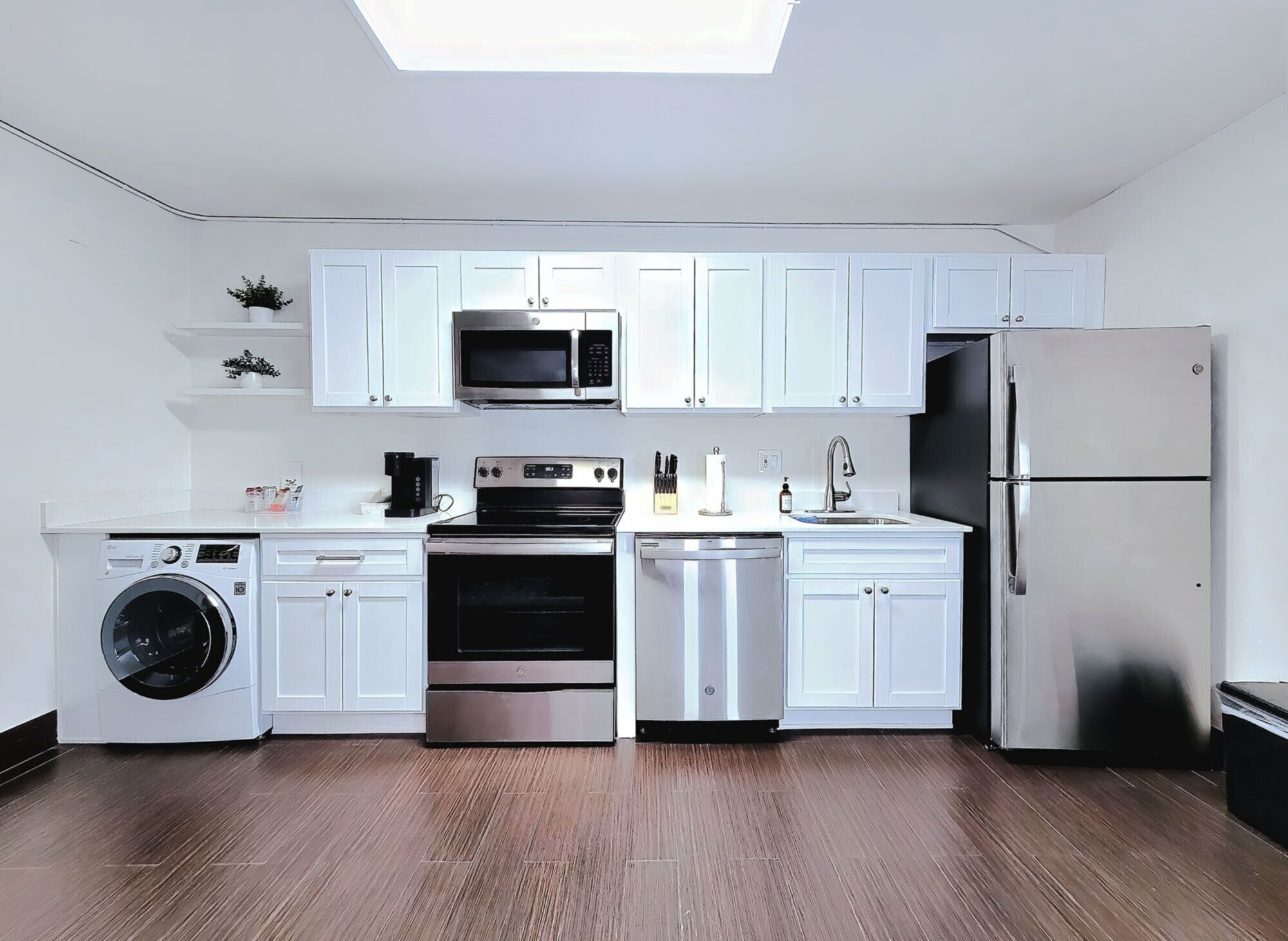 Una cucina moderna con mobili bianchi, microonde, forno, lavastoviglie e frigorifero.