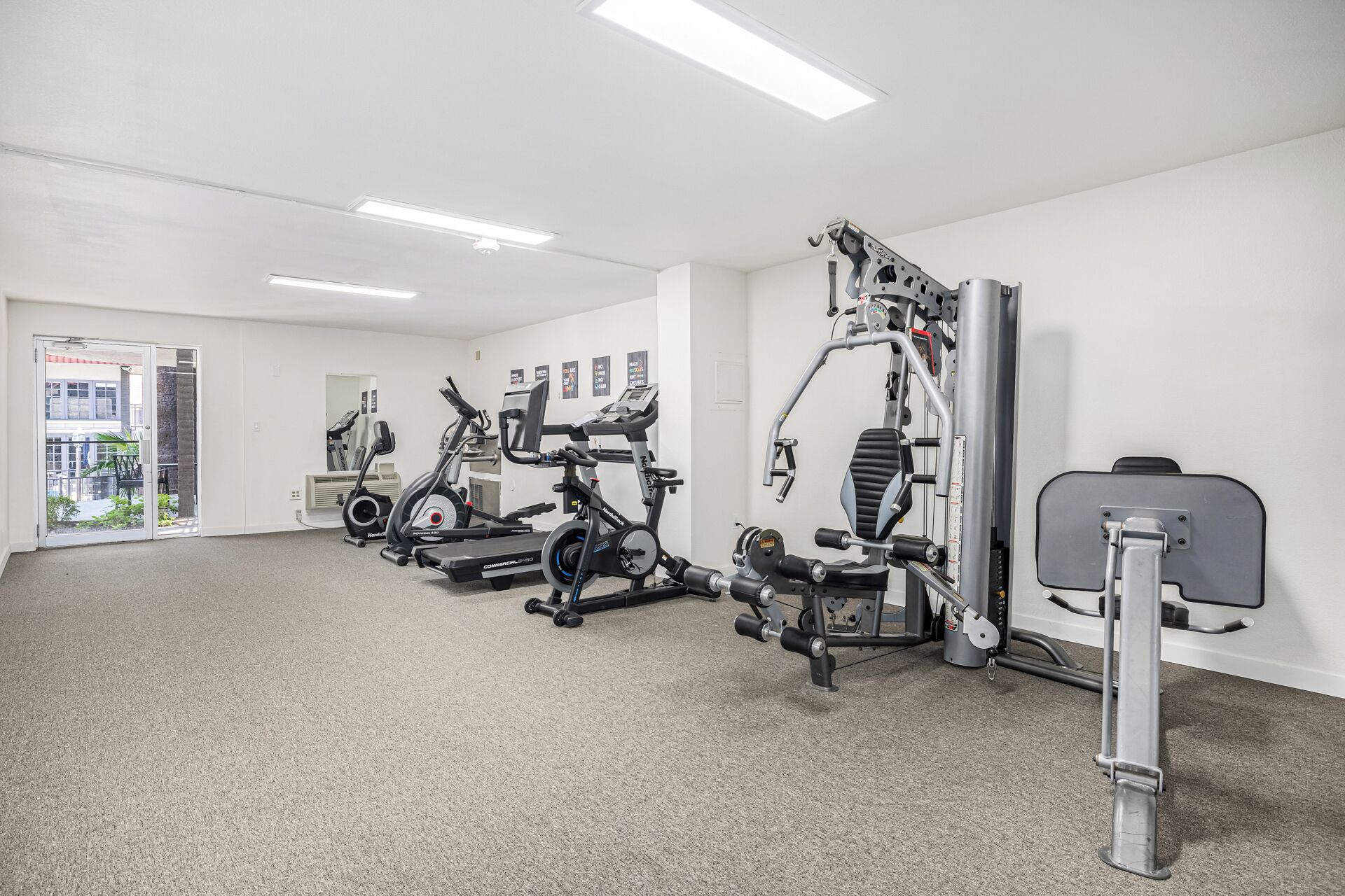 Un gimnasio con máquinas de cardio, equipo de levantamiento de pesas y una puerta que da a un balcón.