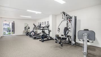 Un gimnasio con máquinas de cardio, equipo de levantamiento de pesas y una puerta que da a un balcón.