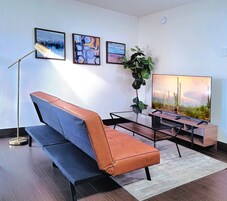 Una sala de estar moderna con un sofá, una lámpara de pie, un televisor y obras de arte enmarcadas en la pared.