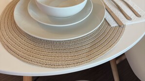 Une table à manger dressée avec de l’assiette blanche, des bols, des couverts et un set de table en fibres tressées.