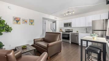 A modern kitchen with white cabinets, stainless steel appliances, and a dining area with a bar stool.
