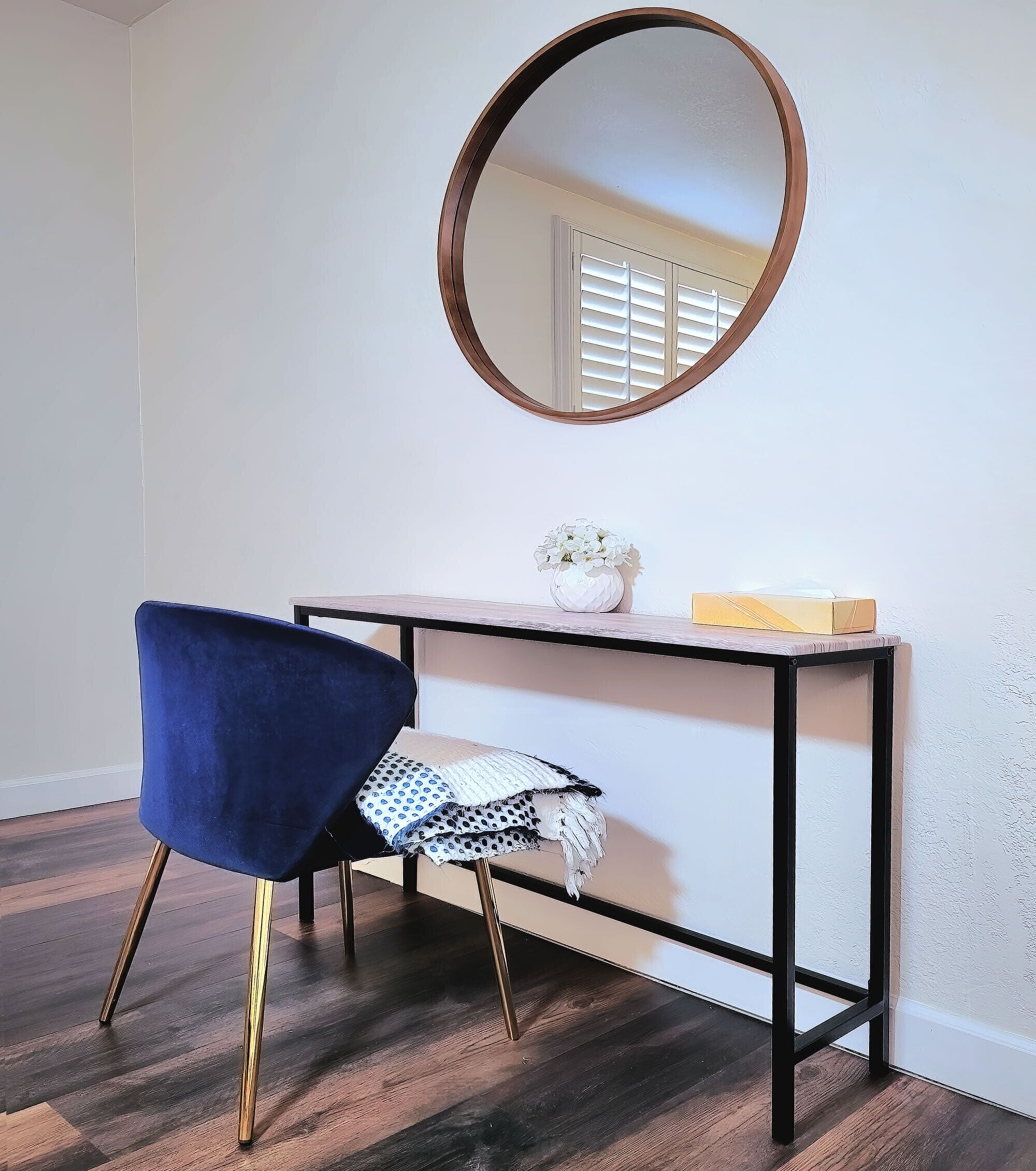 A room with a desk, a chair, a round mirror, and a window with blinds.