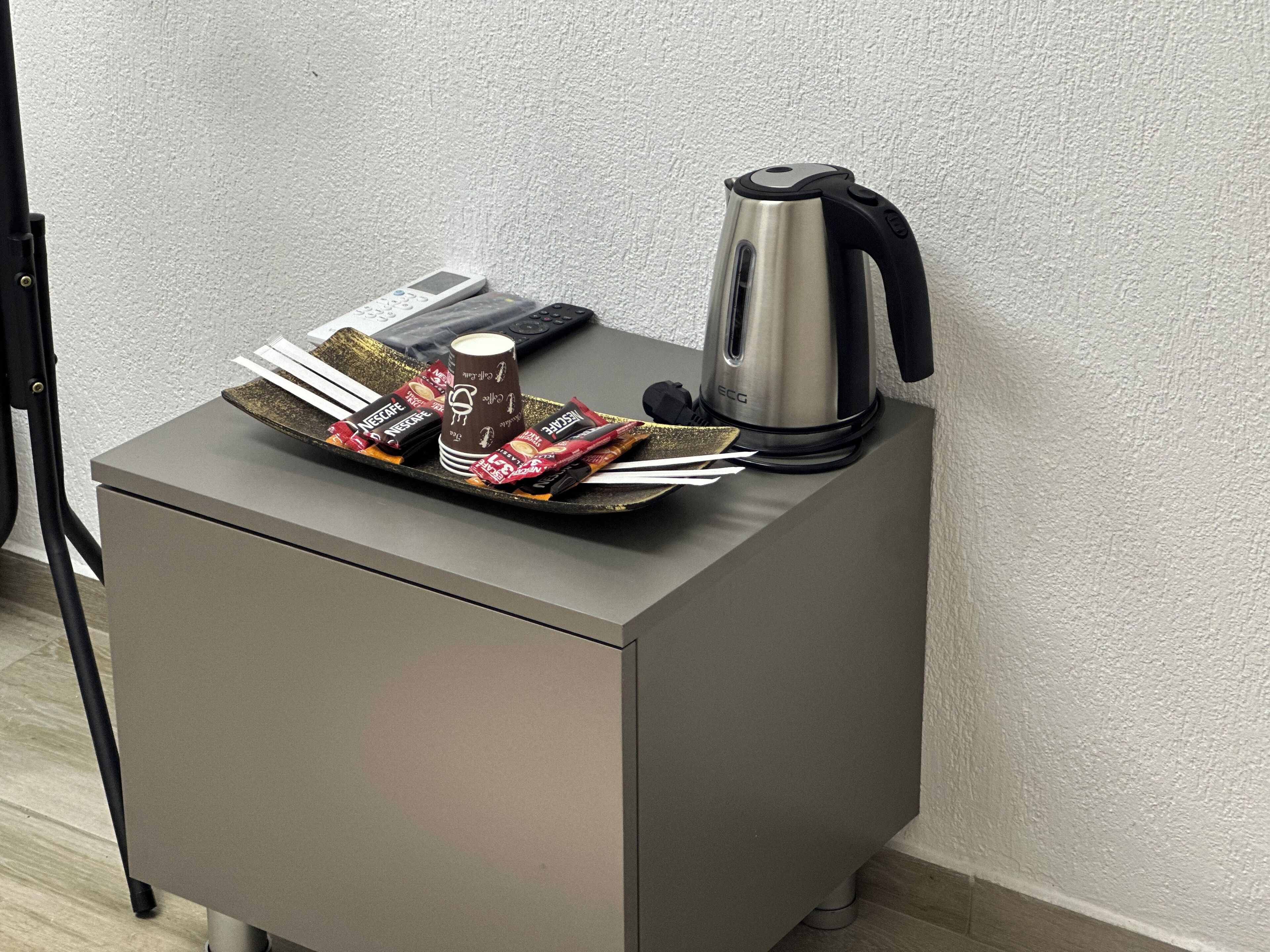 A small kitchenette with a coffee maker, a remote control, and a tray of snacks.