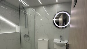 Ein modernes Badezimmer mit einer Duschkabine, einer Toilette, einem Waschbecken und einem Spiegel mit runder Beleuchtung.
