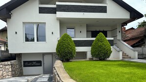 Ein modernes, zweistöckiges Haus mit Eingangsbereich in Steinoptik, einem gepflegten Rasen und zwei gleichmäßig angeordneten Bäumen.