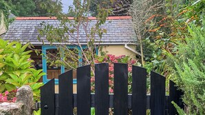 A black wooden gate with a metal latch, a stone wall, and a house with a red roof and blue trim.