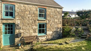 A stone house with a blue door and windows, a bench, and a garden.