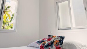 A bedroom with a bed, a hanging light fixture, and two windows with white frames.