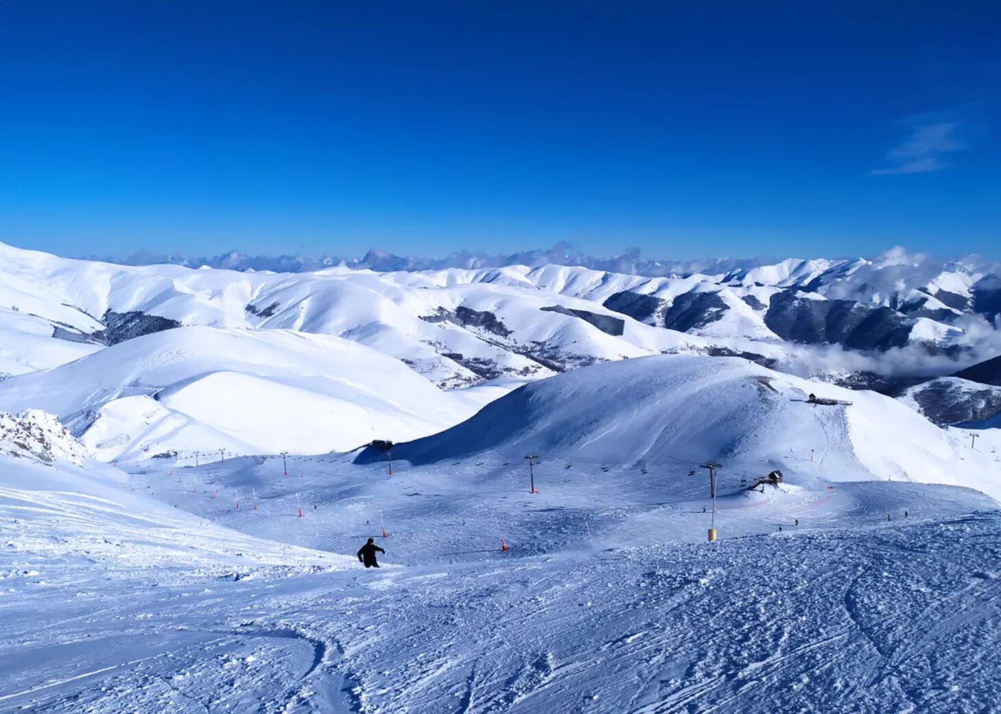 Paisaje nevado de montañas con pistas de esquí y un cielo azul despejado.