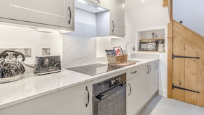Una cocina moderna con armarios blancos, horno integrado y hervidor de acero inoxidable.