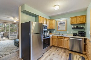 A modern kitchen with stainless steel appliances, wooden cabinets, and a sliding glass door leading to an outdoor patio. - Peaceful Cabin on Whitefish Chain (Crosslake)