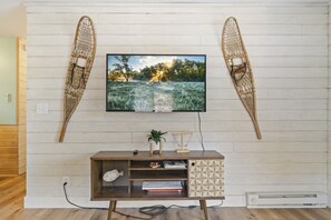 A living room with a television mounted on a white wall, a wooden entertainment unit below, and two decorative wall hangings.