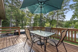 A wooden deck with a glass table and chairs, an umbrella, and a view of a lake. - Peaceful Cabin on Whitefish Chain (Crosslake)