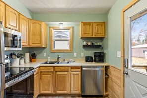 A compact kitchen with wooden cabinets, a stainless steel dishwasher, a microwave, and a coffee maker. - Peaceful Cabin on Whitefish Chain (Crosslake)