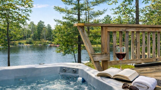 Un bain à remous avec une terrasse en bois, un verre de vin rouge, un livre et une serviette.