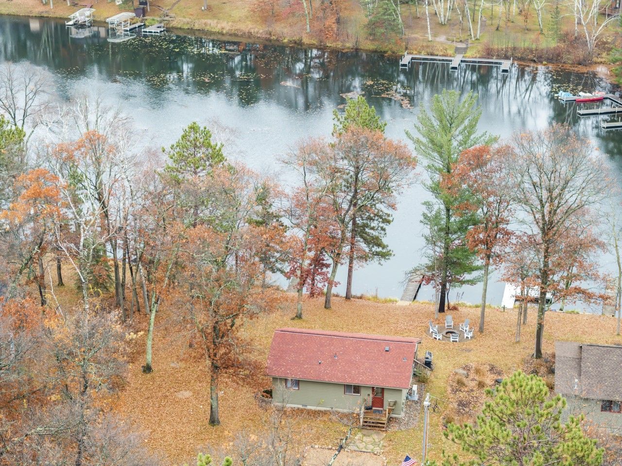 A lakeside cabin with a dock, surrounded by trees with autumn foliage.