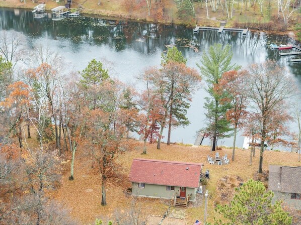 A lakeside cabin with a dock, surrounded by trees with autumn foliage.