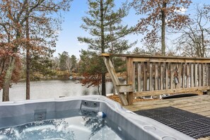 A hot tub with a wooden deck and a view of a lake surrounded by trees. - Peaceful Cabin on Whitefish Chain (Crosslake)