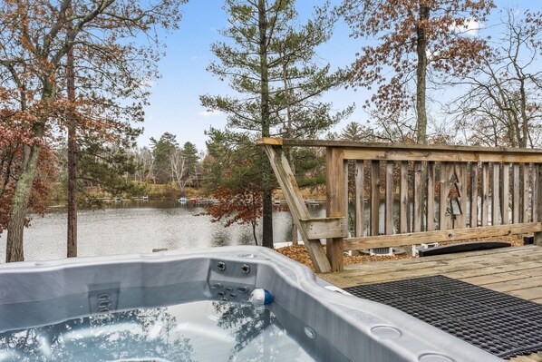 A hot tub with a wooden deck and a view of a lake surrounded by trees. - Peaceful Cabin on Whitefish Chain (Crosslake)