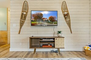 A living room with a mounted TV, wooden walls, a wooden floor, a TV stand with a geometric pattern, and a basket on the floor.
