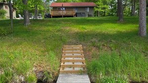 Une terrasse en bois qui mène à une maison entourée de pelouse et d’arbres.