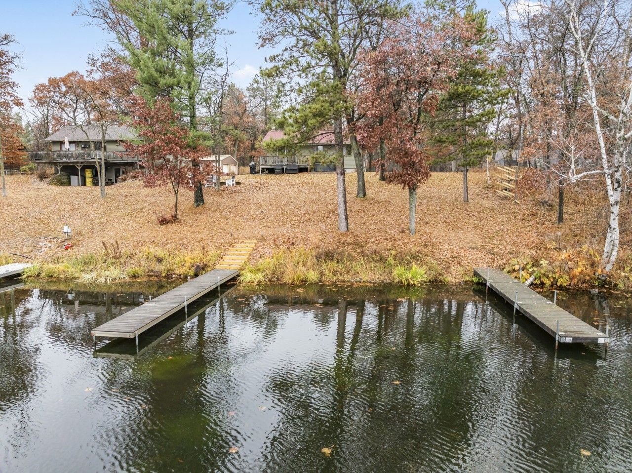 Un lac paisible avec des quais en bois, entouré d’arbres et avec une maison visible au loin.