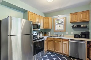 A kitchen with stainless steel appliances, wooden cabinets, a window, and a coffee maker on the countertop. - Peaceful Cabin on Whitefish Chain (Crosslake)