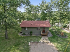 A single-story house with a red roof, surrounded by a well-maintained lawn and trees. - Peaceful Cabin on Whitefish Chain (Crosslake)