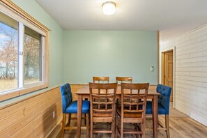 A dining area with a wooden table and chairs, a window with blinds, and a light fixture on the ceiling.