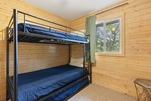 Habitació amb literes, parets de fusta, una finestra amb vista a arbres i un petit tamboret.