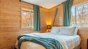 Une chambre confortable dans un chalet, avec un grand lit, des murs en bois et une fenêtre avec des rideaux.