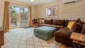 Un salon spacieux avec un canapé en cuir marron, un pouf assorti et une table basse en bois. Une grande porte-fenêtre coulissante donne accès à un patio extérieur.