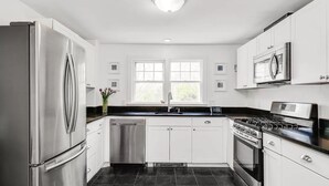 A modern kitchen with stainless steel appliances, white cabinetry, and a black tiled floor. - 2 bedroom house in W Falmouth, Directly on Shining bike path, bike 2 beach. (Falmouth)