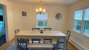 A dining room with a white table, blue chairs, a chandelier, and a rug with a nautical theme. - 2 bedroom house in W Falmouth, Directly on Shining bike path, bike 2 beach. (Falmouth)