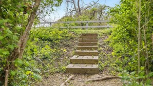 A wooden staircase leading up a hill, surrounded by greenery and trees. - 2 bedroom house in W Falmouth, Directly on Shining bike path, bike 2 beach. (Falmouth)