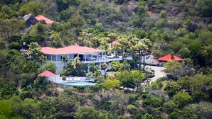 Ein großes, mehrstöckiges Haus mit rotem Dach, umgeben von dichter Vegetation und einem Schwimmbad.