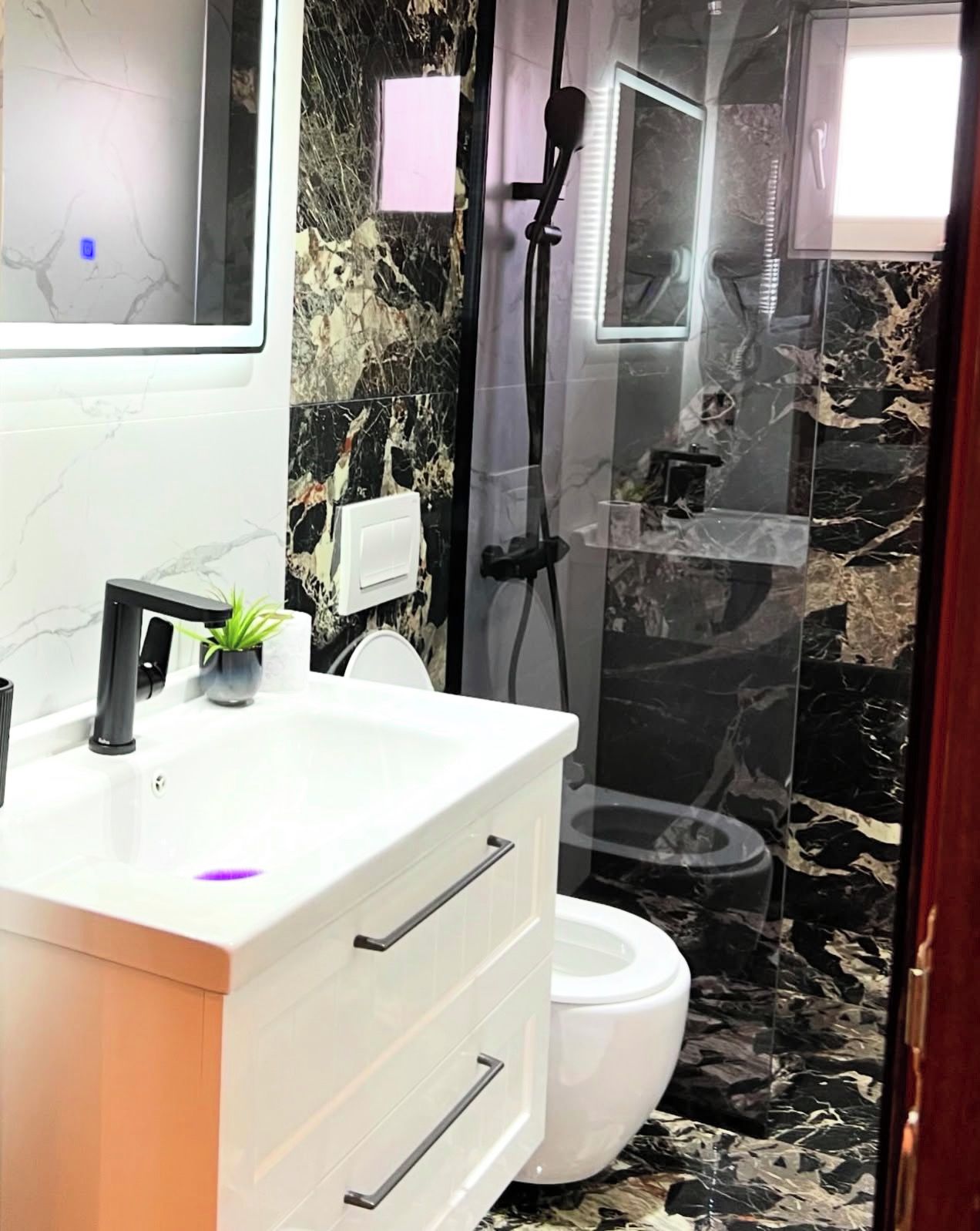 A modern bathroom with a white vanity, a toilet, and a shower area with a glass door.
