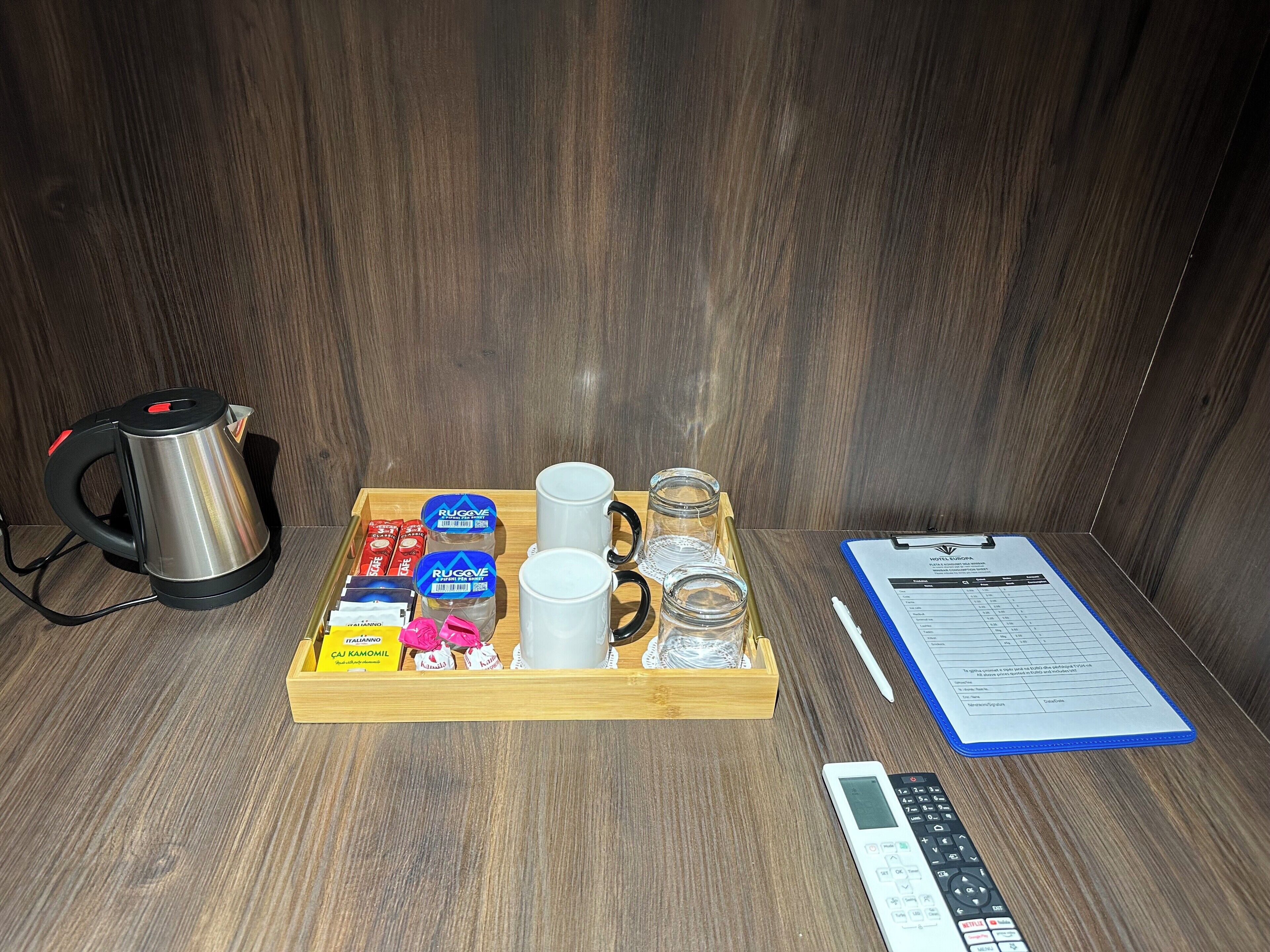 Una bandeja con una tetera, tazas, tarros y un menú sobre una mesa de madera.