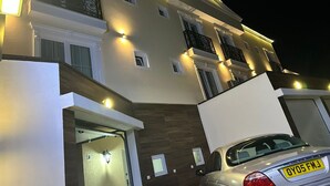 Een meerlaags woongebouw met buitenverlichting, een auto op de oprit, en het cijfer '2' op de deur.