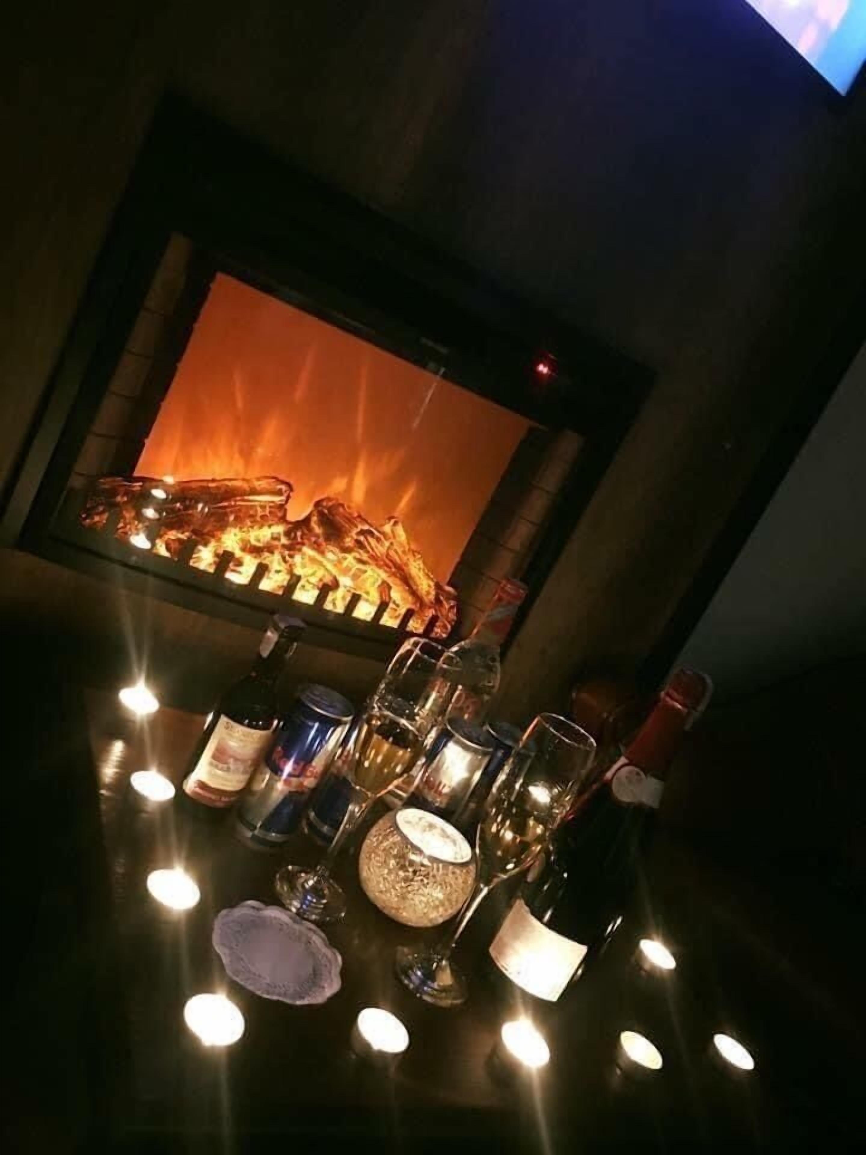 A bar area with a fireplace, bottles, glasses, and a candle on the table.