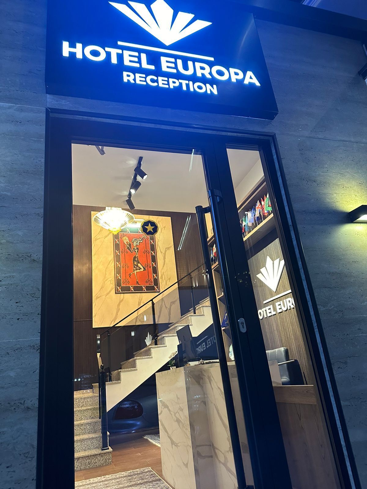 La entrada a la recepción del Hotel Europa, con un diseño moderno que incluye un puerta de vidrio, una escalera y un mostrador de recepción.