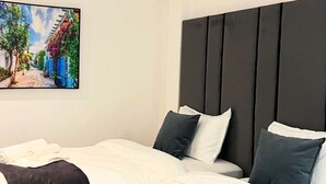 Een hotelkamer met twee bedden, een groot schilderij van een straatbeeld en een donker hoofdeinde.