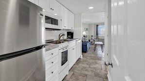 Una cocina moderna con armarios blancos, electrodomésticos de acero inoxidable y piso de baldosas.