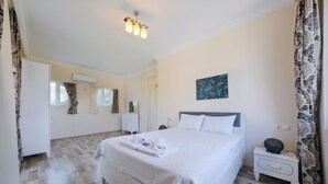 A bedroom with a bed, bedside tables, a nightstand, a wall-mounted air conditioner, and a window with curtains. - Villa Maya (Fethiye)