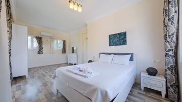 A bedroom with a bed, bedside tables, a nightstand, a wall-mounted air conditioner, and a window with curtains.