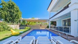 A swimming pool with lounge chairs, a covered patio, and a view of a house. - Villa Maya (Fethiye)