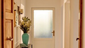 Ein Flur mit einer Milchglasschiebetür, einem Blumenstrauß in einer Vase, einem Teppich und einem kleinen Tisch mit Büchern.