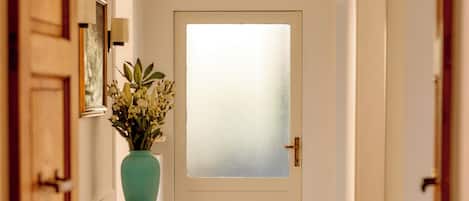 A hallway with a frosted glass door, a vase with flowers, a rug, and a small table with books.