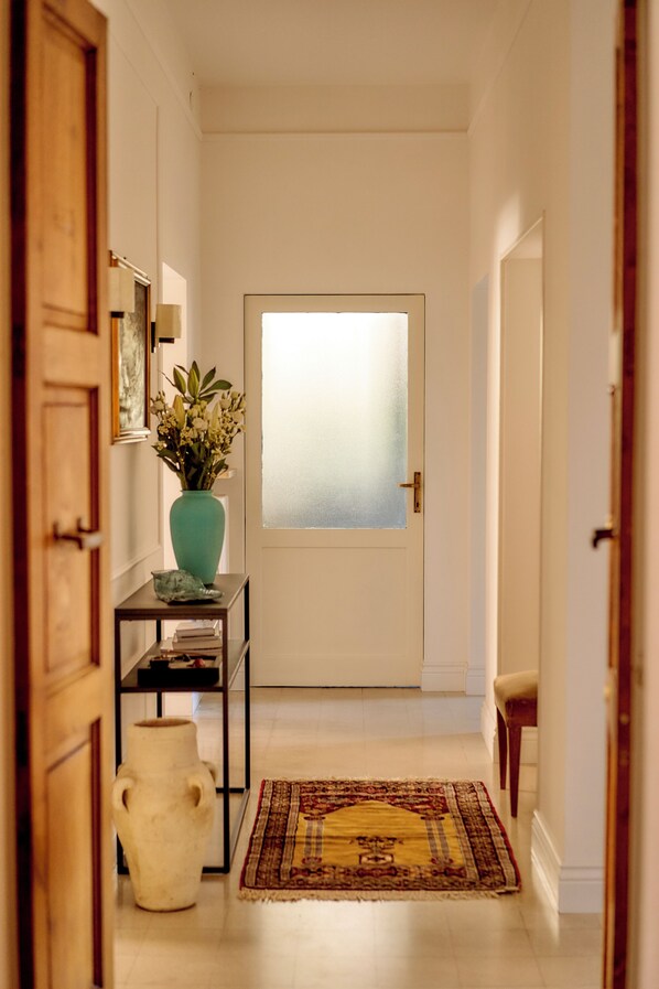 A hallway with a frosted glass door, a vase with flowers, a rug, and a small table with books.